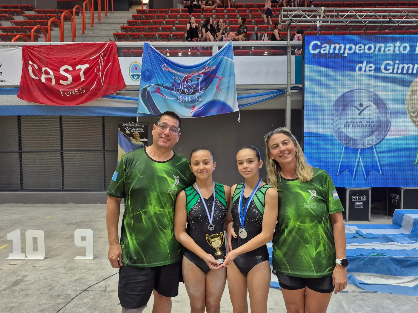 Gimnastas con medallas y trofeo junto a su familia, representando a la Federación Neuquina de Gimnasia